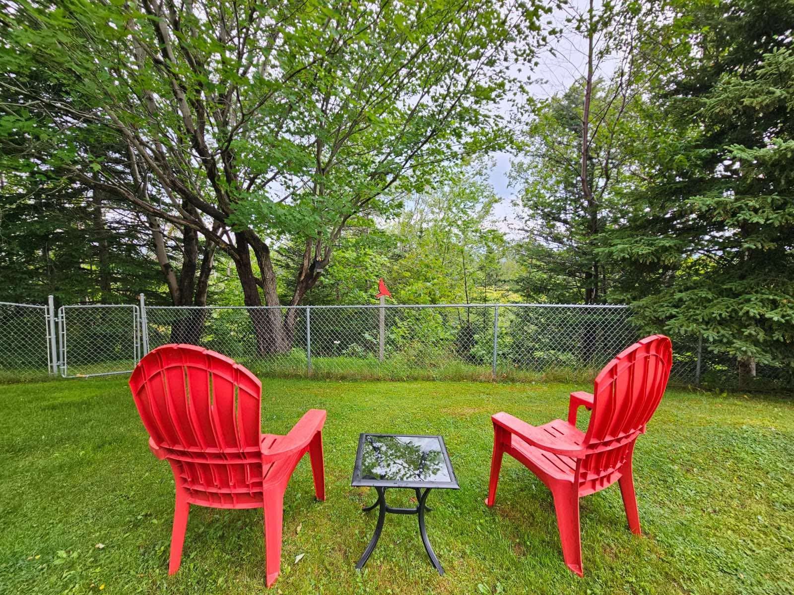 Private fenced backyard with two red Adirondack chairs and a small side table under mature trees